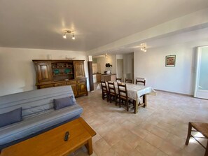 A living room with a sofa, a dining table with chairs, a kitchen area, and a large window. - South Ardeche: gite 2 bedrooms, air conditioning, wifi, swimming pool, Near Vallon Pont d'arc (Balazuc)