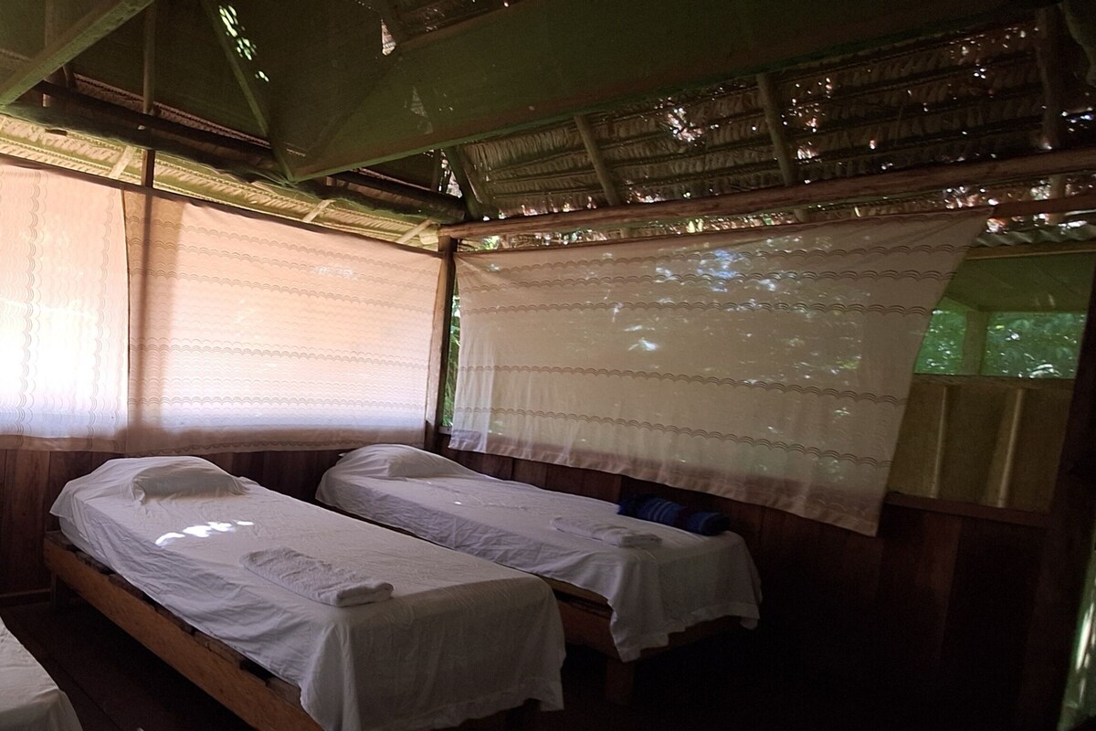Una habitación con dos camas individuales, cabeceros de madera y una ventana con cortinas traslúcidas.