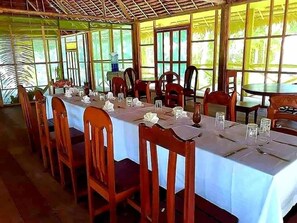 A dining area with tables set for multiple people, chairs, and a water dispenser. - Amazon Tropical Expeditions (Iquitos)