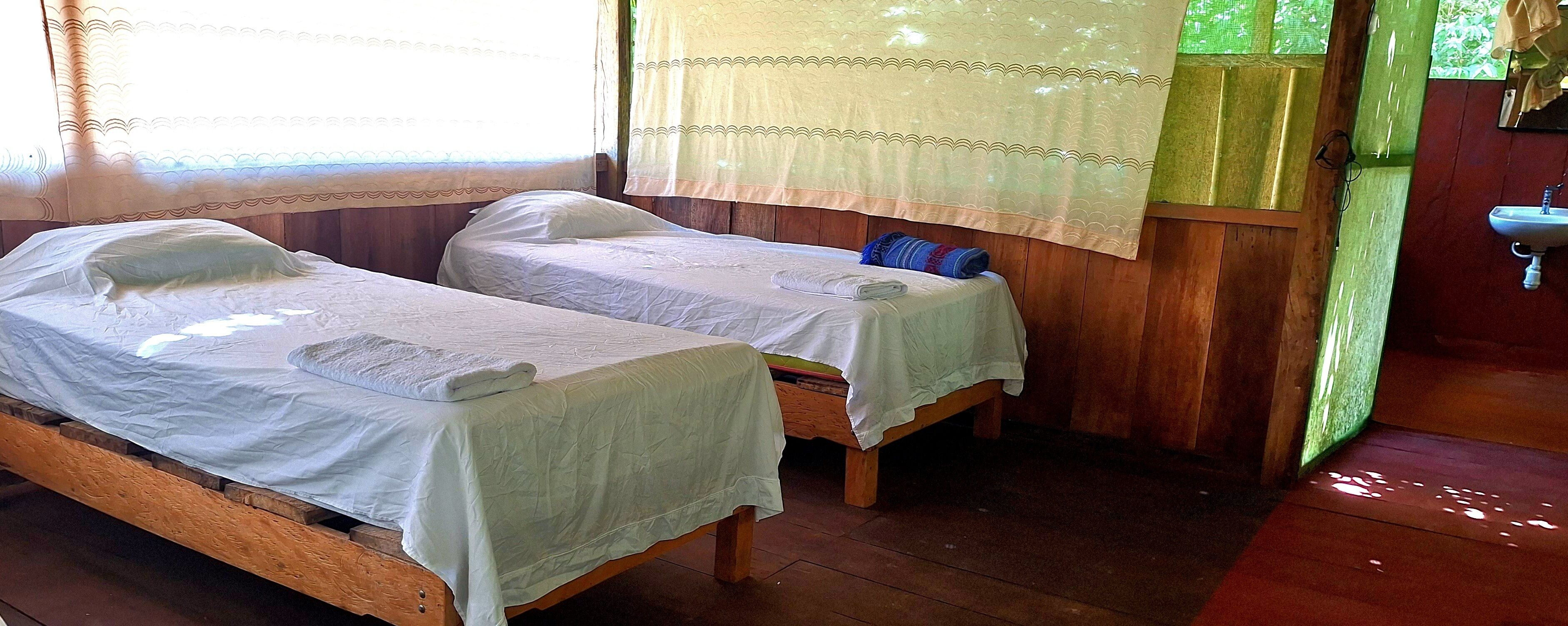 Two single beds with white linens, wooden headboards, and a small table between them.