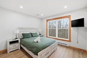 Camera da letto con un letto, comodini, una TV e una finestra vista alberi.