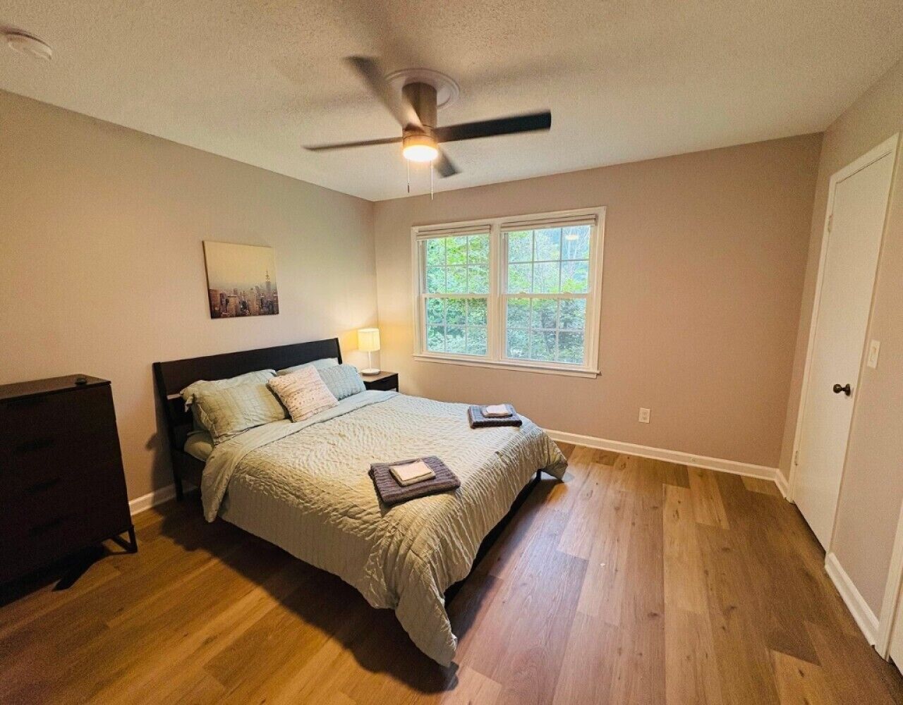 Ein Schlafzimmer mit Bett, Nachttisch, Kommode, Deckenventilator und Fenster.