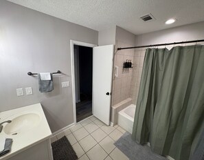 Ein Badezimmer mit einem weißen Waschbecken, einer Duschvorhangstange und einer Tür zu einem weiteren Raum.
