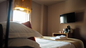 A hotel room with a bed, a television mounted on the wall, and a small table with a coffee maker. - Family King Room with Attached Single Room (Bude)