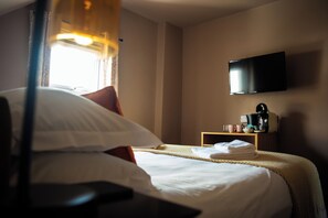 A hotel room with a bed, a television mounted on the wall, and a small table with a coffee maker. - Family King Room with Attached Single Room (Bude)