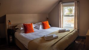 A hotel room with a large bed, two pillows, a bedside table with a lamp, and a window with curtains. - Family King Room with Attached Single Room (Bude)