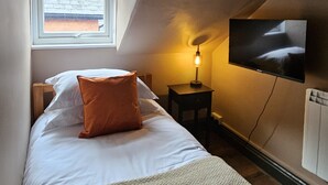 A bedroom with a bed, a TV mounted on the wall, a window, and a nightstand. - Family King Room with Attached Single Room (Bude)