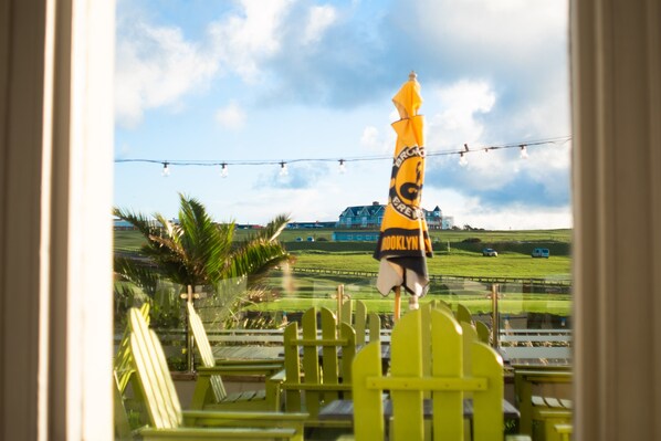 A view through a window with a yellow umbrella, outdoor seating, and a distant building.