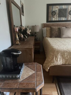 Una habitación de hotel con una cama, cafetera, mesita de noche, lámpara y espejo.