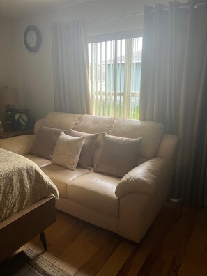 Een woonkamer met een beige bank, een houten salontafel en een raam met gordijnen.