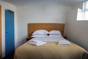 A hotel room with a bed, white pillows, a wooden headboard, a blue door, and a window.