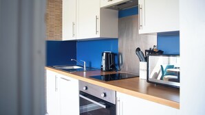 Une cuisine moderne avec des meubles blancs, un pare-feu bleu, un four encastré, une machine à café et un bloc à couteaux.