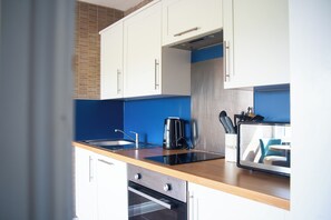 A modern kitchen with white cabinets, a blue backsplash, a built-in oven, a coffee maker, and a knife block.