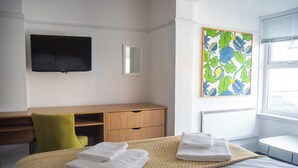 Une chambre d’hôtel avec un lit, un bureau, une chaise, une télévision et une fenêtre.