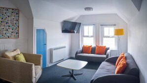 Un salon moderne avec un canapé, un fauteuil et un téléviseur à écran plat fixé au mur.
