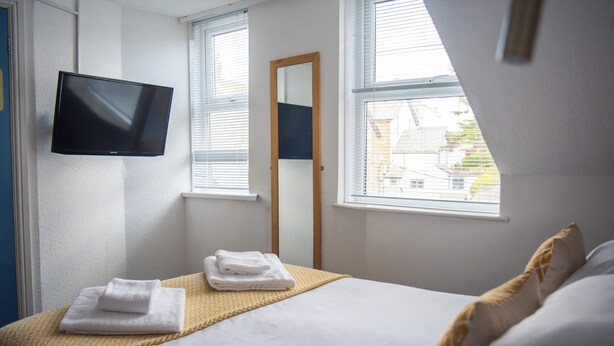 Habitación de hotel con cama, televisor de pantalla plana en la pared, ventana con persianas y un espejo.