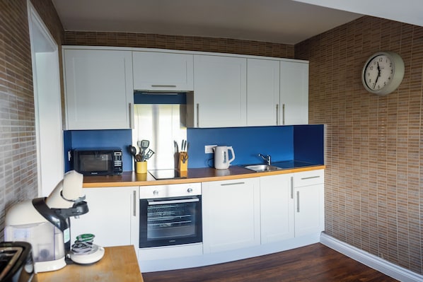 A kitchen with white cabinets, a microwave, an oven, a sink, and a clock on the wall.