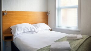 Een net opgemaakt bed met witte lakens, een houten hoofdbord en een deken met een groen patroon.