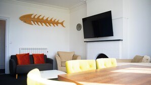 Een moderne woonkamer met een eettafel, gele stoelen, een bank en een flatscreen televisie die aan de muur is bevestigd.