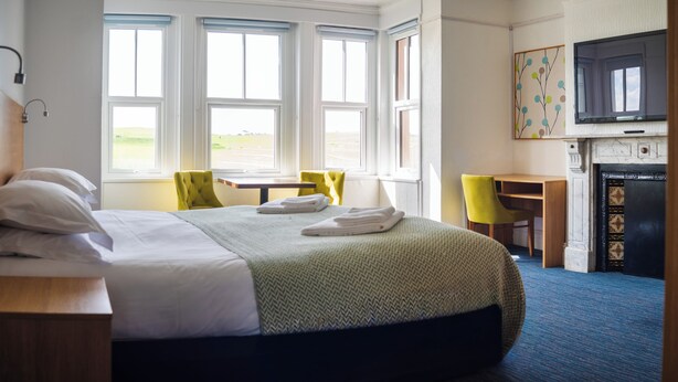 Een hotelkamer met een bed, een bureau, een stoel, een televisie en een open haard.
