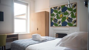 Una camera da letto con un letto, una scrivania, una sedia, un camino e un quadro floreale.