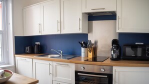 Una cucina con mobili bianchi, un piano di lavoro in legno, un lavello, una macchina da caffè, un forno a microonde e un forno.