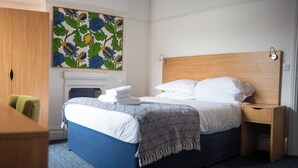 Una camera d'albergo con un letto, un comodino, una sedia, un armadio in legno e un'opera d'arte appesa al muro.