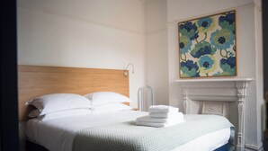Un letto ben rifatto con lenzuola bianche, una testata in legno e una coperta a motivi verdi.