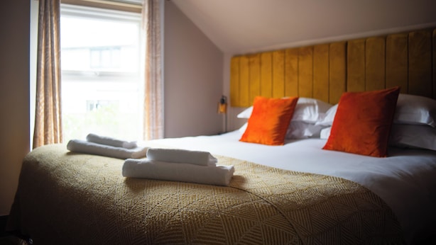 Una habitación de hotel con cama, almohadas, una ventana con cortinas y cabecera.