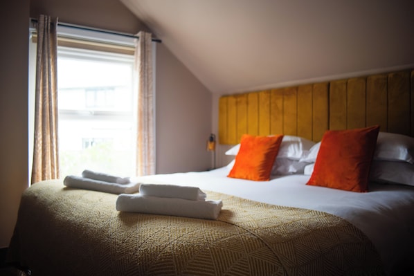 Hotellihuone, jossa on sänky, tyynyt, ikkuna verhoilla ja sängynpääty.