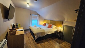 Una habitación de hotel con cama, escritorio con lámpara, televisor y ventana.