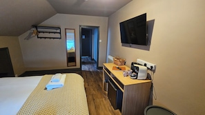 A hotel room with a bed, a desk with a coffee maker, a TV, and a mirror.