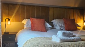 Una cama bien hecha con almohadas, una lámpara de noche y una toalla enrollada sobre la cama.