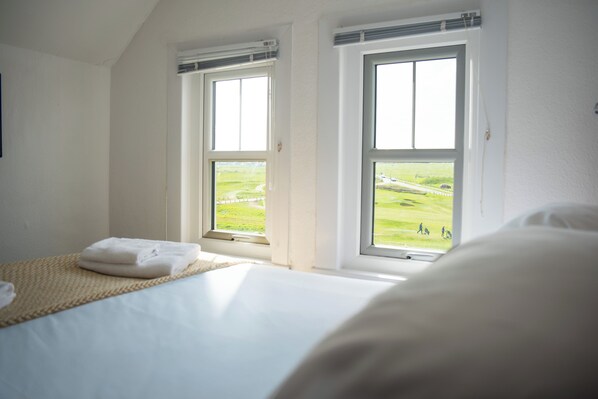 Un dormitorio con dos ventanas, una cama y vistas a un paisaje verde.