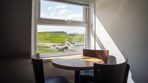 Ein Zimmer mit Fensterblick auf eine grüne Landschaft, einem runden Tisch und zwei Stühlen.