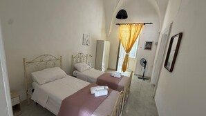 A bedroom with two beds, a standing fan, and a window with curtains.