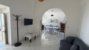A modern living room with a sofa, a coat rack, a TV, and a dining area with chairs and a table.