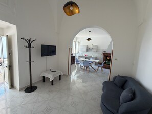 A modern living room with a sofa, a coat rack, a TV, and a dining area with chairs and a table.