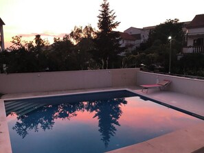 Ein rechteckiger Swimmingpool mit deutlicher Spiegelung von Bäumen und einem Sonnenuntergang.
