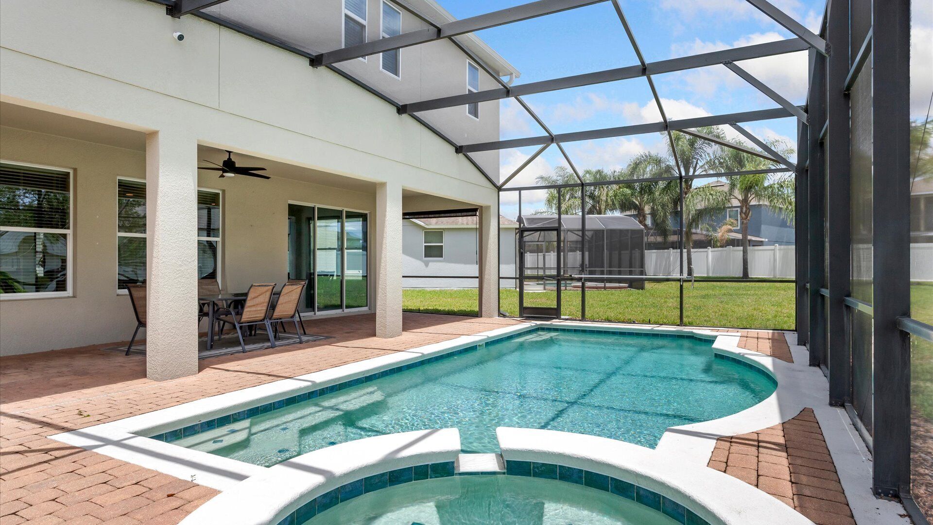 A swimming pool with a covered patio area, a seating arrangement, and a view of the backyard.