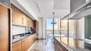 Una cocina moderna con una isla grande, electrodomésticos de acero inoxidable y vistas a un paisaje urbano a través de amplias ventanas.