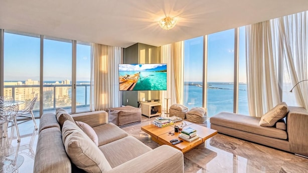 Una sala de estar moderna con un televisor grande, asientos cómodos, una mesa de centro y vista al mar.