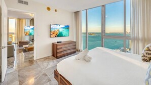 Habitación de hotel con una cama grande, televisión, cómoda de madera y vista al mar.