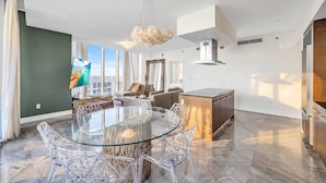 Una sala de estar moderna con una mesa de comedor de vidrio, sillas traslúcidas, un sofá y un televisor.