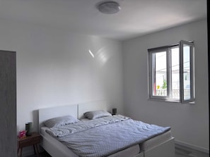Ein Schlafzimmer mit einem Bett, Nachttischen, einem Fenster und einer Deckenleuchte.