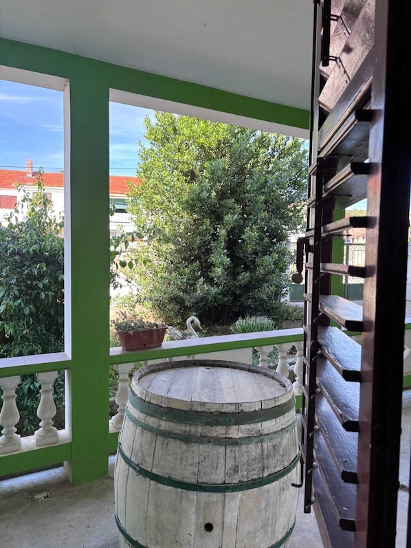 Ein Balkon mit einem Holzbottich, einer grünen Geländer und Blick auf Bäume und Gebäude.