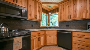 Una cucina con mobili in legno, piano cottura in acciaio inossidabile, microonde e lavastoviglie.