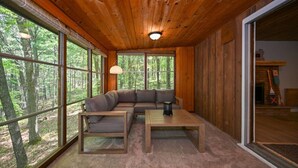 Un interno in legno con un divano componibile, un tavolino da caffè e ampie finestre con vista sulla foresta.
