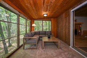 Ein Holzinnenraum mit einer Eckcouch, einem Couchtisch und großen Fenstern mit Blick auf einen Wald.