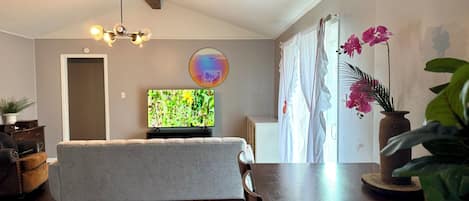 A living room with a sofa, a TV, a wooden ceiling, a dining table, and a potted plant.